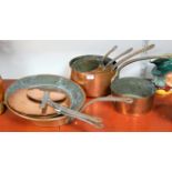 A graduated set of four copper pans each with iron handle, together with a copper saucepan, one