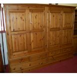 A large modern pine four door wardrobe, having base fitted with four short and two longer drawers,