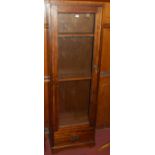 A stained hardwood single door glazed narrow display cabinet, having single lower drawer, width