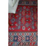 A Turkish woollen red ground rug, having a typical geometric floral decorated ground within trailing