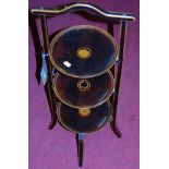 An early 20th century stained walnut and penwork decorated circular three-tier folding cake stand