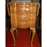 An early 20th century figured walnut serpentine front dropflap three-drawer bedside chest, on
