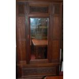 An early 20th century floral relief carved oak single mirrored door wardrobe, having single long