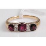 A yellow metal, ruby and diamond ring, arranged as three old cut rubies in a line setting, the