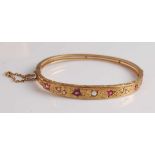 A late Victorian yellow metal, ruby, diamond and seed pearl oval hinged bangle, featuring an