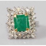 A contemporary white metal, emerald and diamond cluster ring, the four claw set square cut emerald