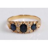 A yellow metal, sapphire and diamond three-stone ring, arranged as a centre oval cut sapphire
