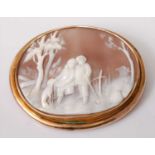 A carved shell cameo brooch in yellow metal mount, depicting a couple and dog within a landscape,