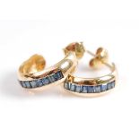 A pair of yellow metal sapphire half-hoop earrings, each featuring nine rectangular cut sapphires in