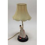 An early 20th century table lamp base, surmounted by china figure in standing pose with fan in hand,