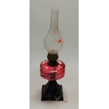 A late Victorian cast iron pedestal oil lamp, lacking shade but with thumb-cut cranberry glass font,