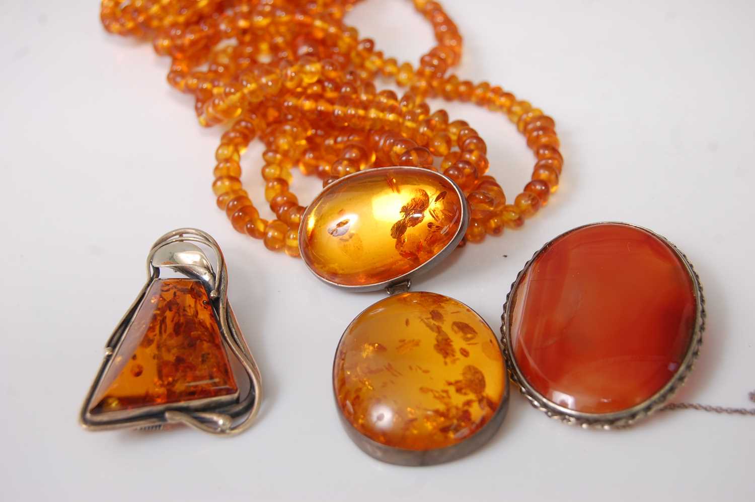 A faux orange amber multi-string necklace with clear amber pendant; together with a silver mounted