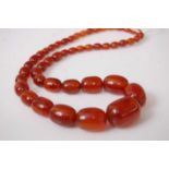 A faux amber necklace, the graduated oval beads between approx 6.7 and 21mm, 70g, gross length 60cm