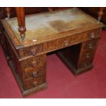 A circa 1900 floral relief and line carved oak kneehole writing desk, having a tooled leather