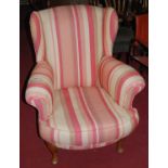 An early 20th century walnut framed and striped upholstered wingback scroll armchair, on cabriole