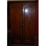 A mid-Victorian mahogany round cornered double door wardrobe, the arched panelled doors enclosing