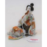 A Japanese porcelain figure of a Geisha, posed with fan to her mouth and in floral decorated robe,