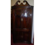 A George III mahogany freestanding four door corner cupboard, having a broken scroll architectural