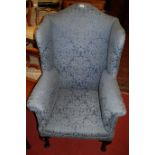 An early 20th century mahogany framed and blue floral upholstered wingback armchair, raised on