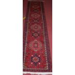 A Persian woollen red ground hall runner, having central geometric floral motifs, 292 x 67cm