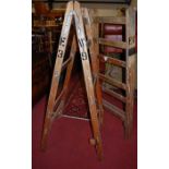 A pair of stained beech and metal bound hinged A-frame ladders