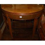 An early 19th century mahogany demi-lune fold-over tea table raised on square tapering supports,