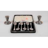 A cased set of six silver teaspoons, together with a pair of silver dwarf candlesticks on loaded