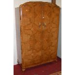 An Art Deco figured walnut double door wardrobe, having polished brass handles and raised on squat