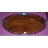 A 19th century mahogany oval serving tray, having raised wavy gallery and twin brass carry