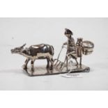A Chinese white metal novelty cruet, in the form of a man driving a bison, on rectangular base