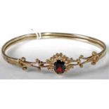 A yellow metal and garnet set hinged bangle (with crude repair), unmarked but tests as approx 9ct,
