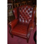 A contemporary tan leather studded and buttoned wingback scroll armchair, raised on square forelegs,