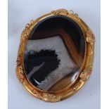 A yellow metal oval banded agate brooch, having a three-dimensional leaf border and hook clasp