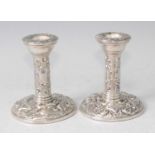 A pair of silver and embossed dwarf candlesticks, each decorated with a bird amidst C-scrolls,