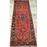A Persian woollen hall runner, the red ground decorated with lozenge medallions within trailing
