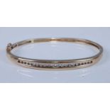 A yellow metal oval hinged hollow diamond bangle, channel set with twenty round brilliant cut
