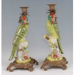 A pair of reproduction porcelain candlesticks, each modelled as a parrot upon a treestump issuing