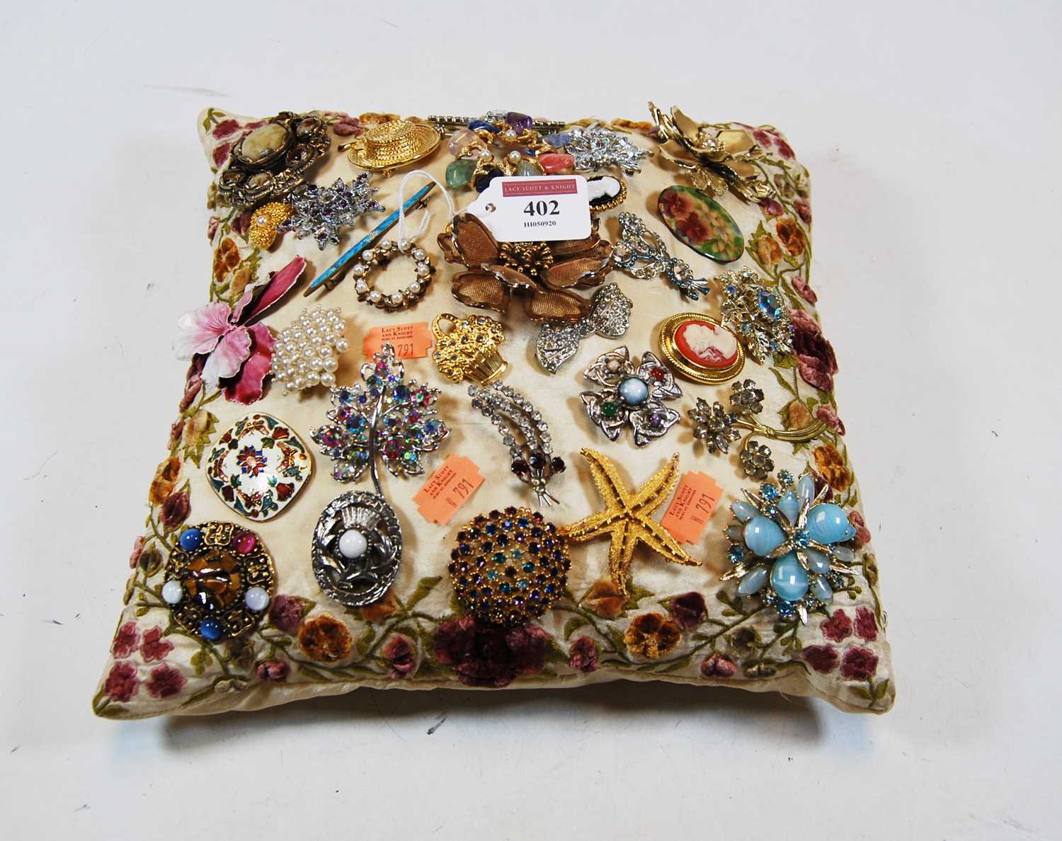A crocheted silk cushion, set with a collection of paste set brooches