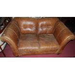 A contemporary tan leather two seater scroll end sofa, raised on turned squat supports, width 163cm