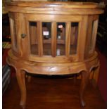 A contemporary hardwood oval single door glazed low drinks cabinet, having removable tray top, w.