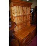 A stained pine kitchen dresser, the two-tier open plate-rack over base fitted with three drawers and