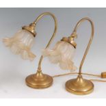 A pair of Art Nouveau brass table lamps, each having shaped floral frosted adjustable shades, raised