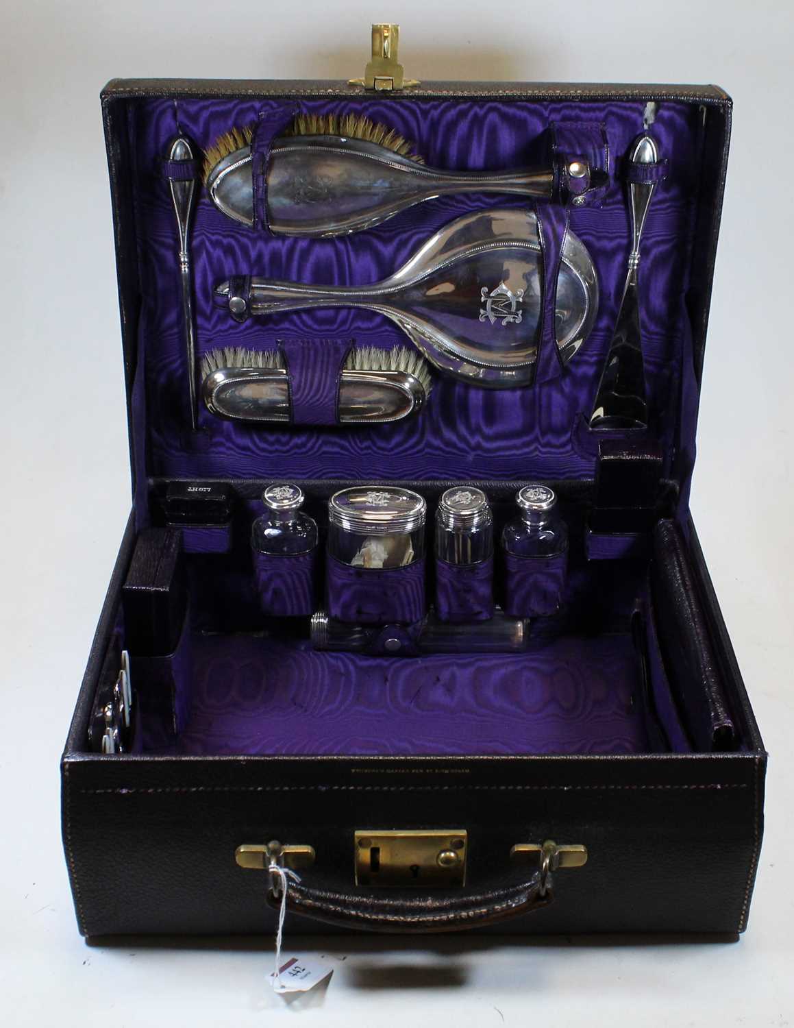 A George V ladies black leather vanity case, the hinged lid opening to reveal a purple silk lined