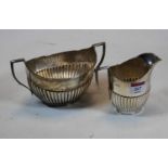 A George V silver twin handled sugar bowl together with a matching cream, each of half-reeded oval