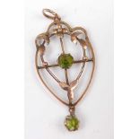 An Edwardian yellow metal openwork shield shaped pendant, with floral detail and two round green