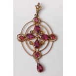 A yellow metal Edwardian openwork garnet and seed pearl pendant, featuring a quartefoil cluster of