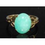 A yellow metal jadeite dress ring, featuring a dyed green oval jadeite cabochon in a four-claw