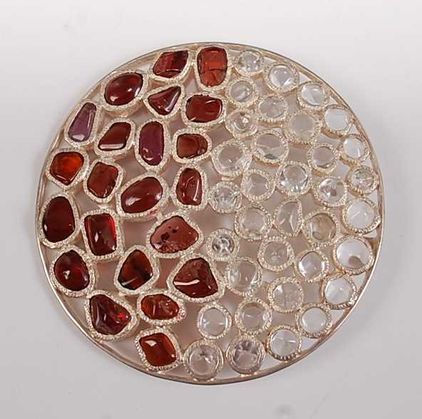 A large sterling silver circular abstract pendant, having 22 polished garnet pieces and 35 rock