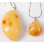 A yellow amber pendant, of good size, on silver finelink neck chain; together with one other similar