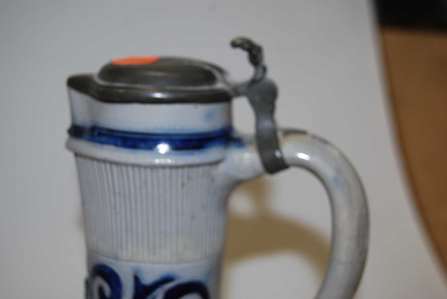 A German Westerwald stoneware jug, with pewter lid and thumb rest decorated in blue with a crucifix, - Image 2 of 14